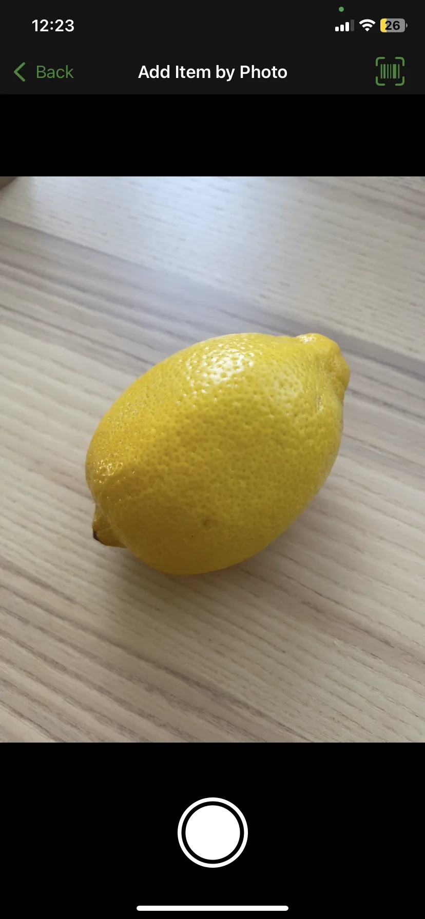 OurGroceries' Add Item by Photo screen, with the camera pointed at a lemon on a wooden table and a shutter button below